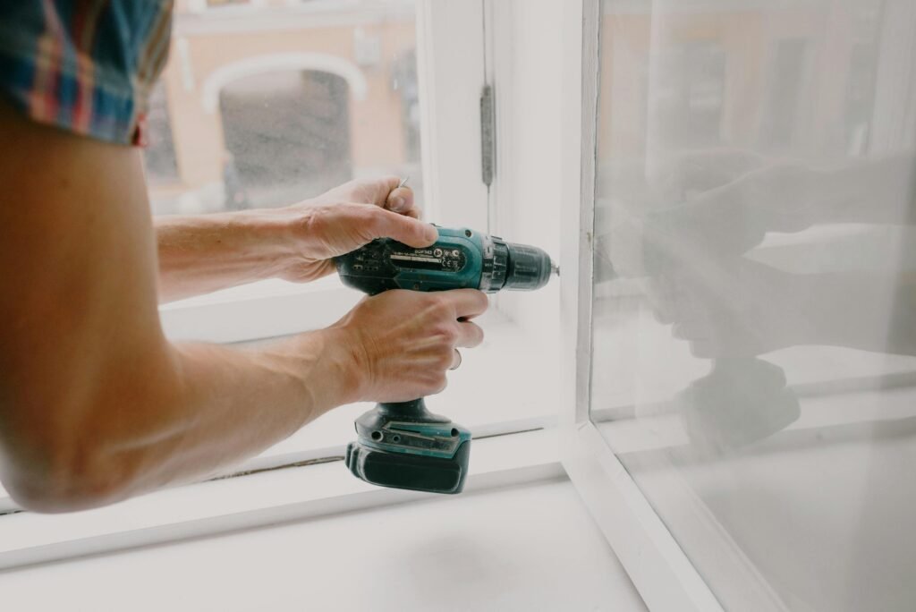 pexels-photo-5768107-5768107 A person using an electric drill to repair or install a window indoors.